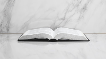 A single open book on a marble tabletop, with a soft reflection visible beneath it.の素材