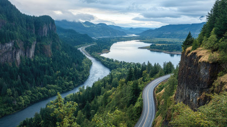 A winding mountain highway overlooking a wide river surrounded by lush forests and steep cliffsの素材