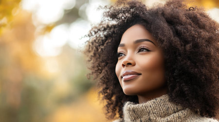 A woman with rich, curly hair, standing outdoors in the fall, wearing a cozy sweater and looking off into the distanceの素材
