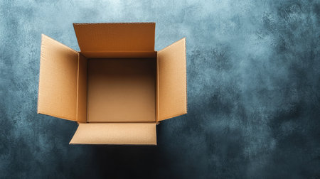 Empty cardboard box, flaps open on a smooth gray surface, ideal for packaging, shipping, or unboxing, showing practical simplicity.の素材