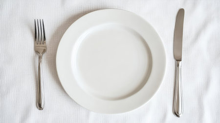 A bright and clean setting with a ceramic plate, fork, and knife laid out separately on a crisp white tableclothの素材