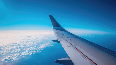 The wing of an airplane soaring above the horizon, with the rich blue sky stretching far into the distance.の素材
