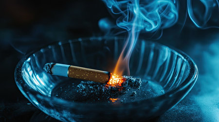 A glowing cigarette ember in a vintage ashtray, the smoke curling into the darkness.の素材