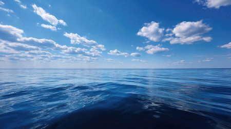 Calm blue sea extending to the horizon with barely a ripple, under a clear, bright sky with just a few clouds scattered aboveの素材