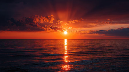 A stunning orange sunset over the sea, with the sun sinking below the horizon, casting brilliant reflections on the waterの素材