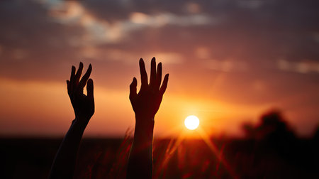 Silhouetted female hands reaching toward the golden setting sun, fingers gently spread to catch the fading lightの素材