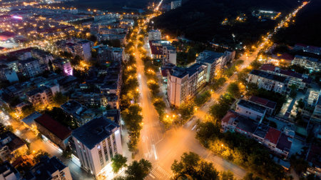 Aerial view of a nighttime city with a network of bright streetlights and illuminated buildings, creating a dynamic and lively urban landscapeの素材