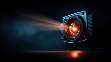 Close-up of a modern movie projector lens glowing in the dark, projecting a film onto the wallの素材