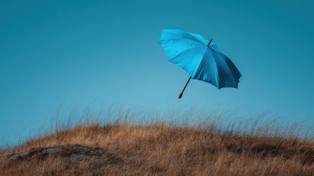Bright blue umbrella flying in the wind over a grassy hill, creating a dynamic and energetic imageの素材