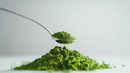 A teaspoon scooping bright green matcha powder from a pile on a crisp white backgroundの素材