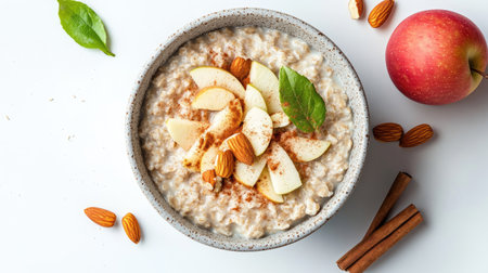 Bowl of oatmeal with cinnamon, apples, and almonds, placed on a white background with minimal shadowsの素材