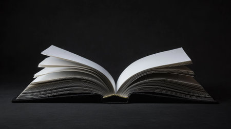 Open book with pristine blank pages lying flat on a deep black background, soft lighting highlighting the paper textureの素材