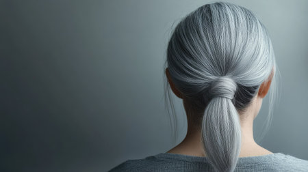 Mature woman's head with long gray hair tied in a bun, soft background highlighting elegance and simplicity.の素材