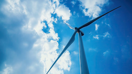 Modern wind turbine with sleek blade design pointing into the sky filled with gentle clouds, symbolizing future energyの素材