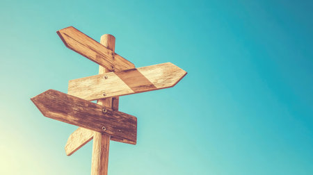 Close-up of blank wooden signpost pointing in different directions, sunny blue sky behind, clean minimalist compositionの素材