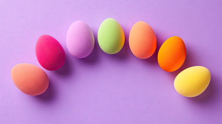 A rainbow of egg-shaped makeup sponges forming a semi-circle on a vibrant purple background.の素材