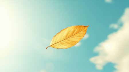 This image captures a solitary orange leaf gently floating against a bright blue sky filled with soft clouds, symbolizing the calmness and transition of autumn.の素材