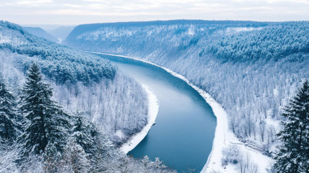 A river winding between snow-covered hills and dense evergreen forests in winter.の素材