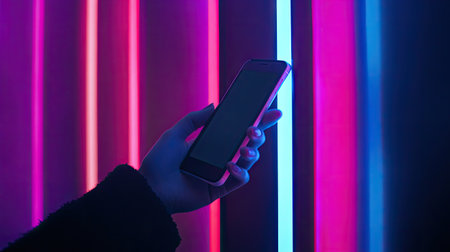 A person's hand using a smartphone to watch a video in landscape mode, glowing screen prominent.の素材