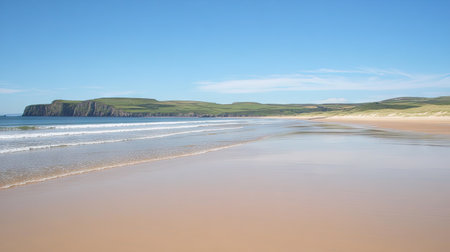 Golden beach sands under clear blue skies with waves gently meeting the shore on a bright, warm day.の素材