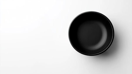 High-angle shot of a simple black bowl on a white background, emphasizing its smooth edges and contemporary design for product or tableware photographyの素材