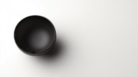 High-angle shot of a simple black bowl on a white background, emphasizing its smooth edges and contemporary design for product or tableware photographyの素材