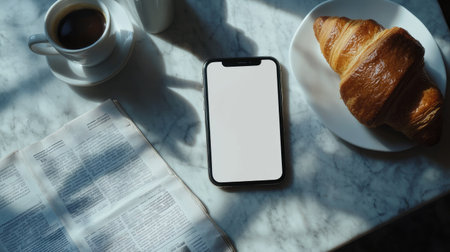 Flat lay of a blank smartphone screen next to a coffee cup, croissant, and morning newspaper on a breakfast tableの素材