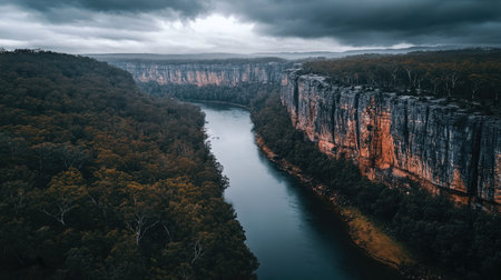 Dramatic aerial view of a winding river flanked by cliffs and dense forest under a moody skyの素材