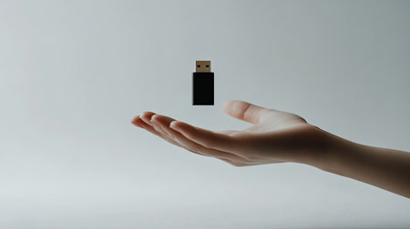 A minimalist view of a hand offering a USB flash drive on a plain white surface.の素材