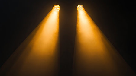 Two warm-toned spotlights overlapping their beams, creating a gradient effect against a black backdropの素材