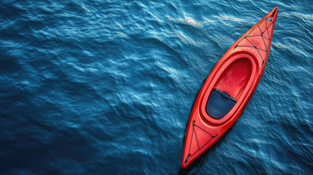 A lone red kayak seen from above, gliding through calm, deep blue ocean waters with rippling waves.の素材