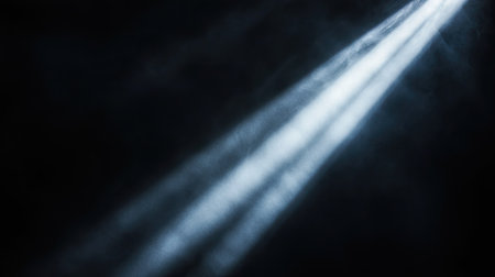 A vibrant shaft of light shining down diagonally from the upper-right corner, illuminating a central focal point in an otherwise black and shadowy scene.の素材