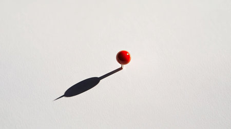 A minimalist composition of a single red pushpin casting a shadow on a bright white background.の素材