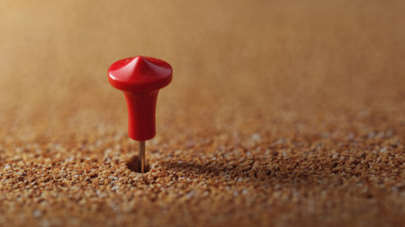 A red pushpin piercing a sheet of paper on a corkboard, with the cork texture in focus.の素材