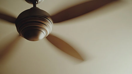 Slow motion shot of a ceiling fan spinning, with focus on the blades and gentle motion blur, against a plain ceiling.の素材
