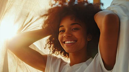 A woman waking up and pulling the covers off, smiling as she gets ready to start her day with energy.の素材