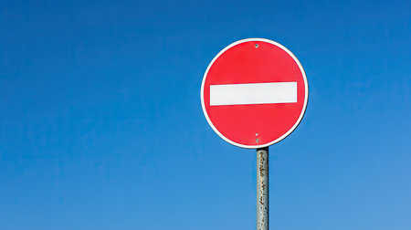 A vivid red stop sign against a clear blue sky represents a no entry policy. This striking image captures road safety and traffic control themes, perfect for various applications.の素材