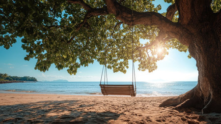 This tranquil beach scene features a wooden swing hanging from a large tree, perfect for relaxation. The clear blue sky and bright sun create an idyllic atmosphere by the shore.の素材