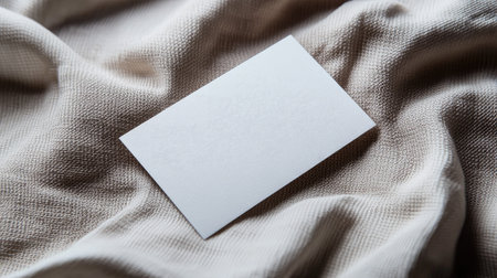 The image showcases a minimalist blank business card lying on a soft textured fabric. This versatile setup suits various branding and identity projects.の素材
