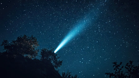 A breathtaking scene showcasing a comet's brilliant trail against a star-filled night sky, with silhouetted trees providing an awe-inspiring natural frame.の素材