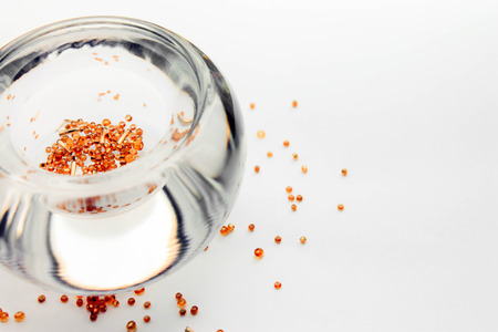 Transparent clear bowl vase glass filled with gold decorative beads on light background closeup