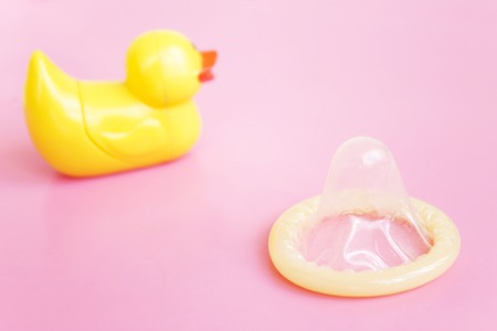 Contraception. Opened condom and yellow toy duckling on pink background with copy spaceの写真素材