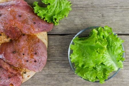 Raw meat with spices and salad leaves in a glass bowl on an old vintage wooden background. Top view.の写真素材