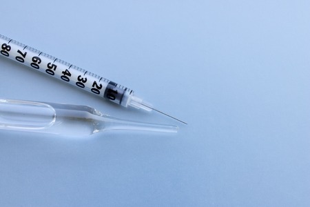 Transparent vial container with liquid medicine near small insulin syringe on blue background....