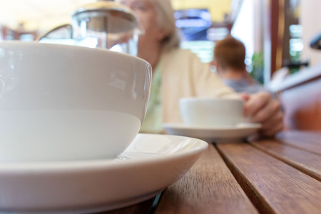 Two teacups and French press on the table, blurred woman behindの写真素材