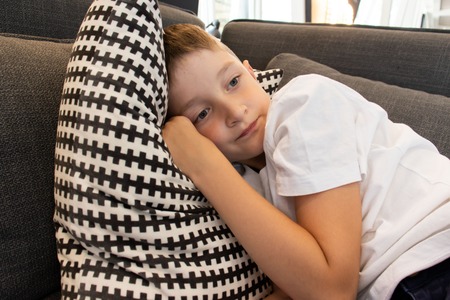 A cute boy lying on sofa and put a head on black and white checkered pillow
