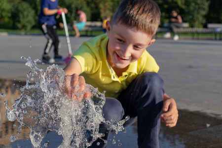 Smiling caucasian boy playing with fountain water in city park.