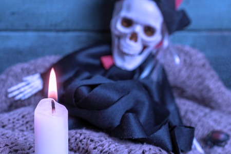 Burning candle and blurred skeleton witch on wooden background, toned in blue. Halloween concept.の写真素材