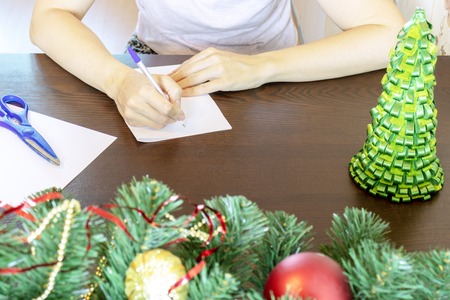 Hands of a woman sitting by the table and writing christmas wishes on a card, letter.の写真素材