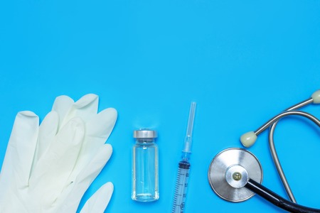 Layout of medical equipment, gloves, syringe, vial and stethoscope on blue background with copy...